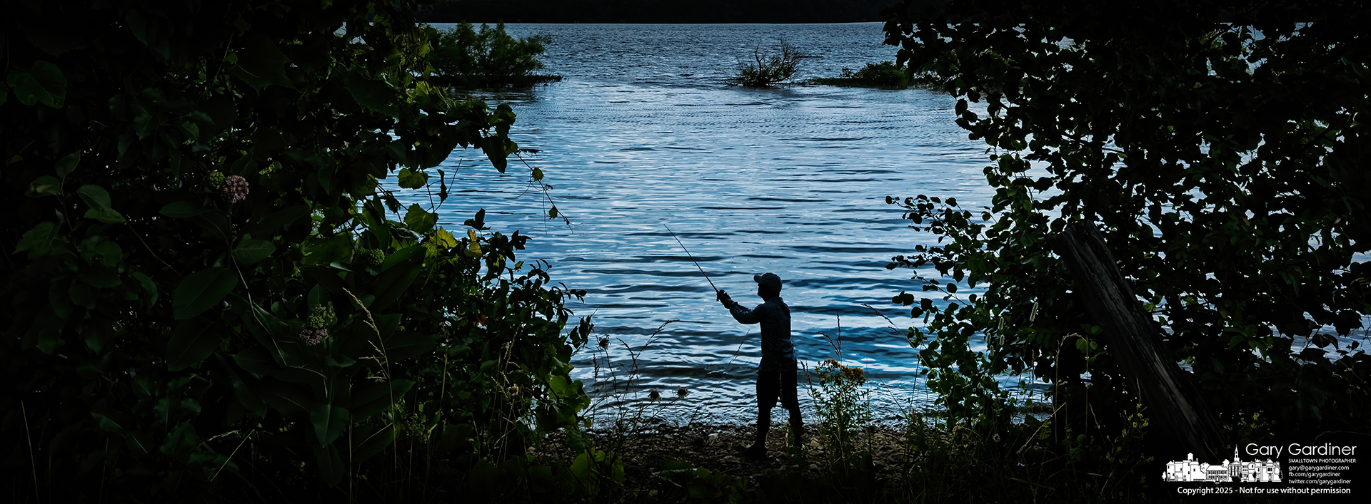 A fisherman casts his lure into the flooded lagoon at the Walnut Street boat ramp as the sky darkens under an afternoon rainstorm. My Final Photo for June 25, 2025.