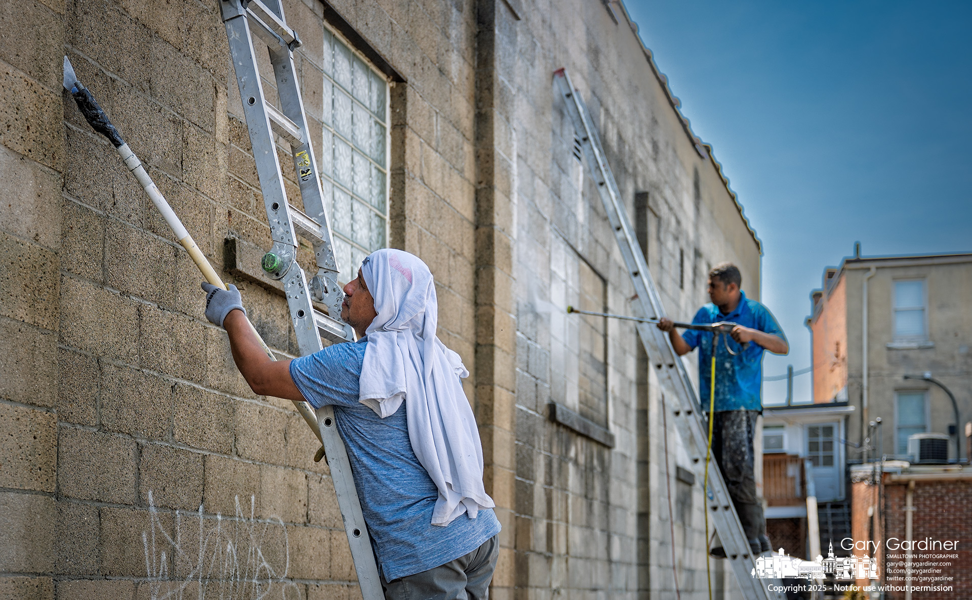 A work crew power washes and scrapes the north wall of Amish Originals in Uptown, preparing the surface for repairs and sealing.. My Final Photo for July 30, 2025.