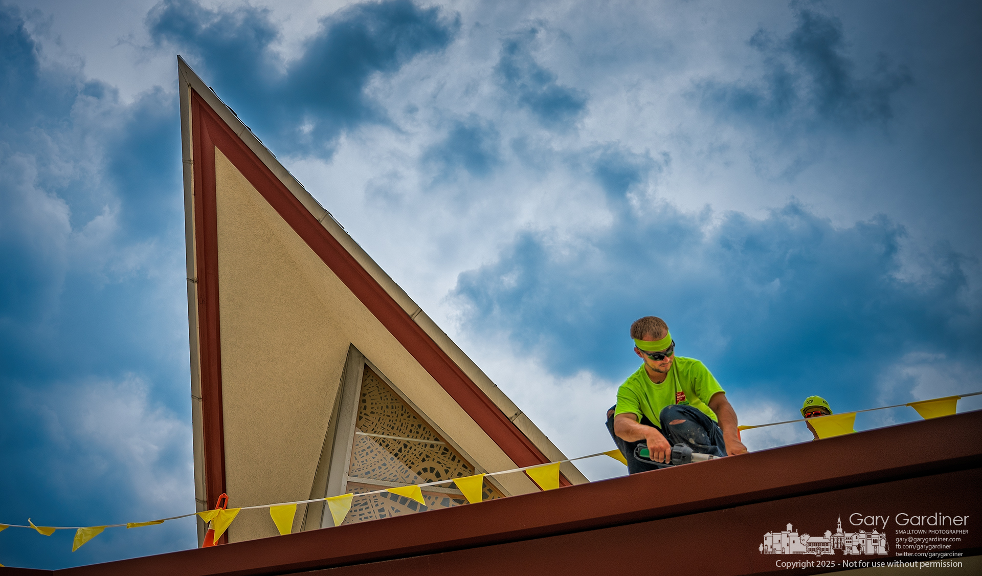 At the Church of the Messiah, a worker leans over the edge, carefully trimming the final layer of the new roof above the first floor. My Final Photo for July 9, 2025.