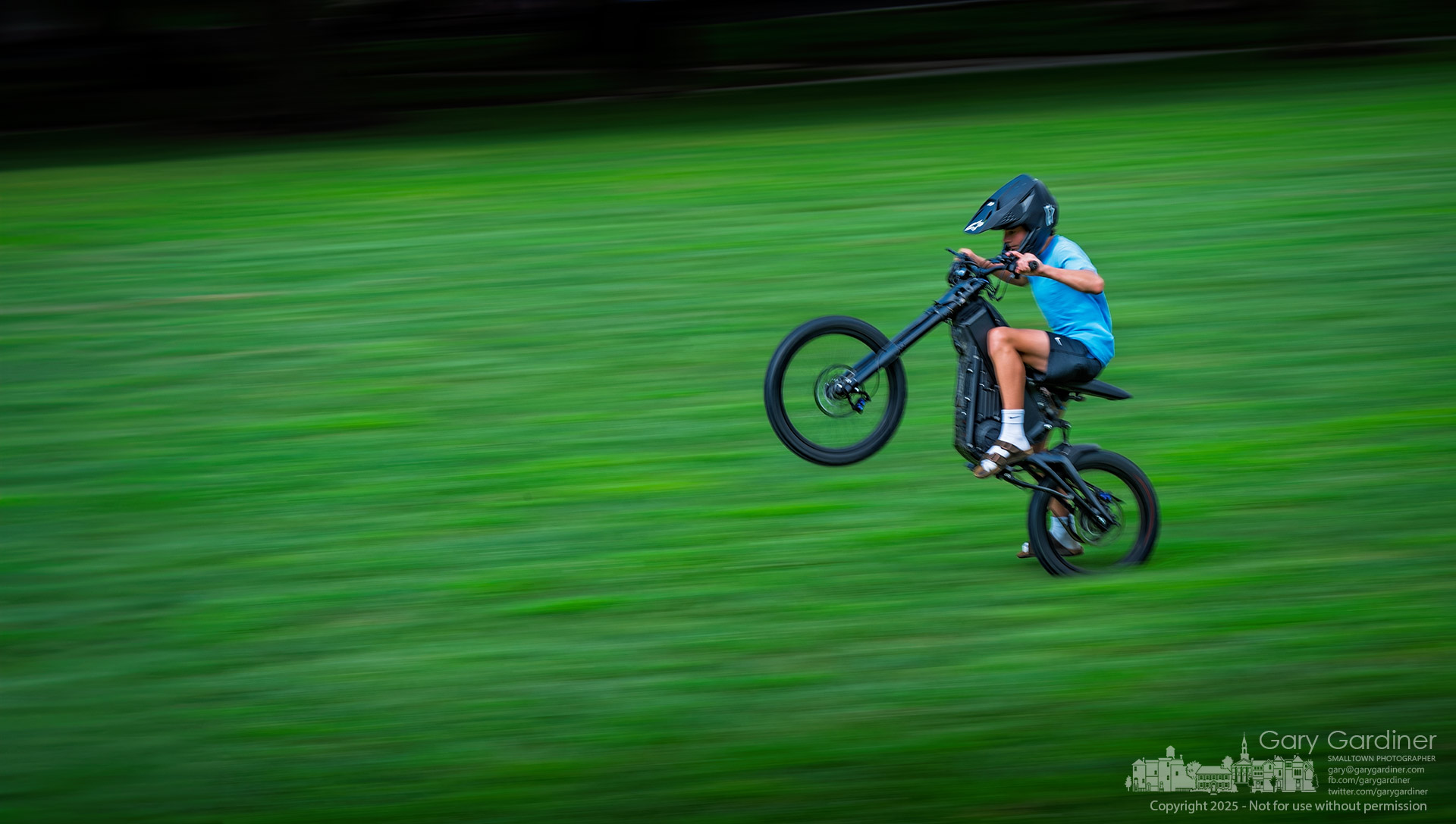 A young cyclist pulls wheelies while riding the new electric bike he purchased with money earned cutting grass and neighborhood odd jobs, using the grassy field at Alum Creek Park as his test track.