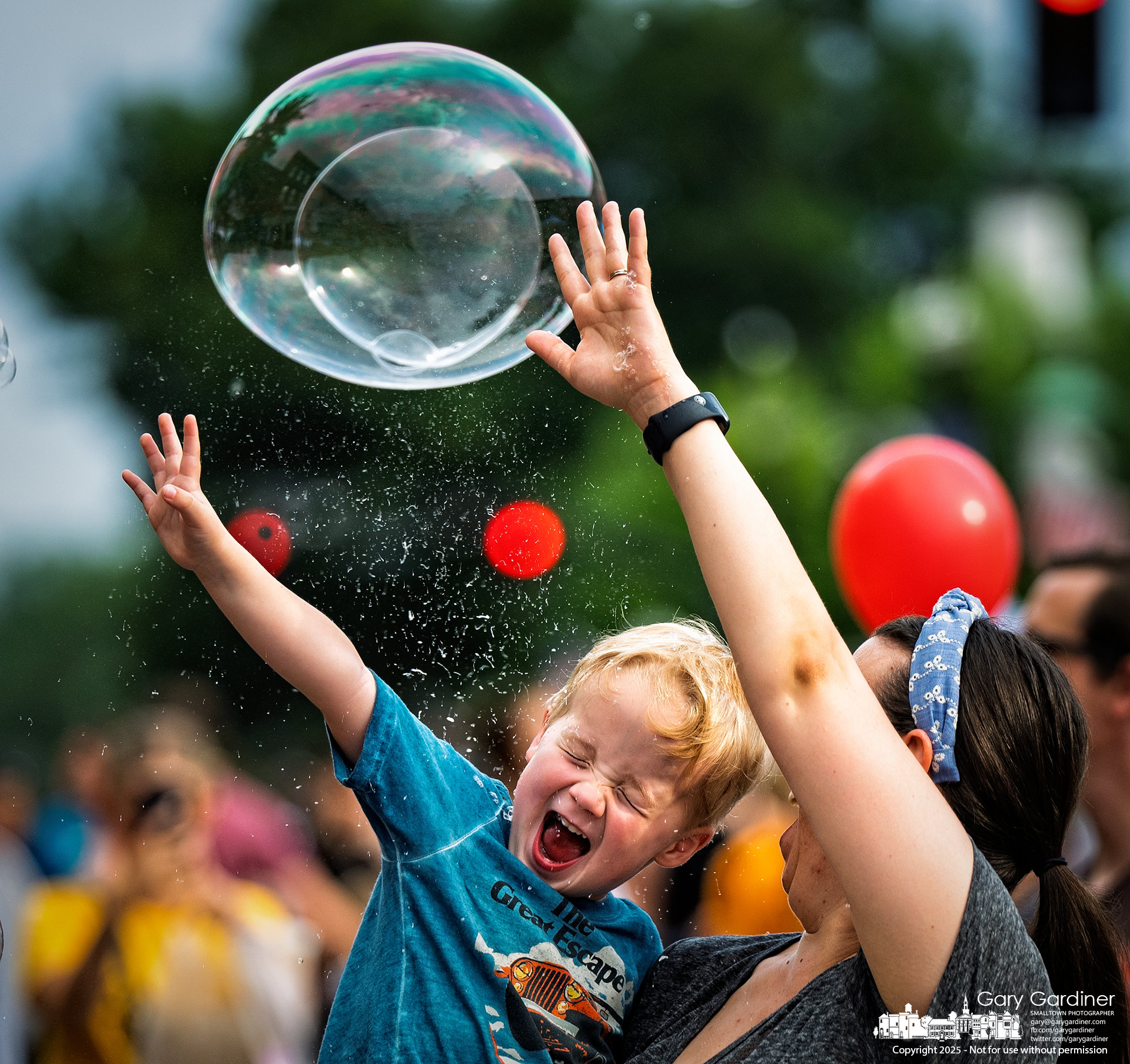 A youngster shares with his mother the joy of popping bubbles blown by a street performer at Fourth Friday in Uptown Westerville. My Final Photo for July 25, 2025.