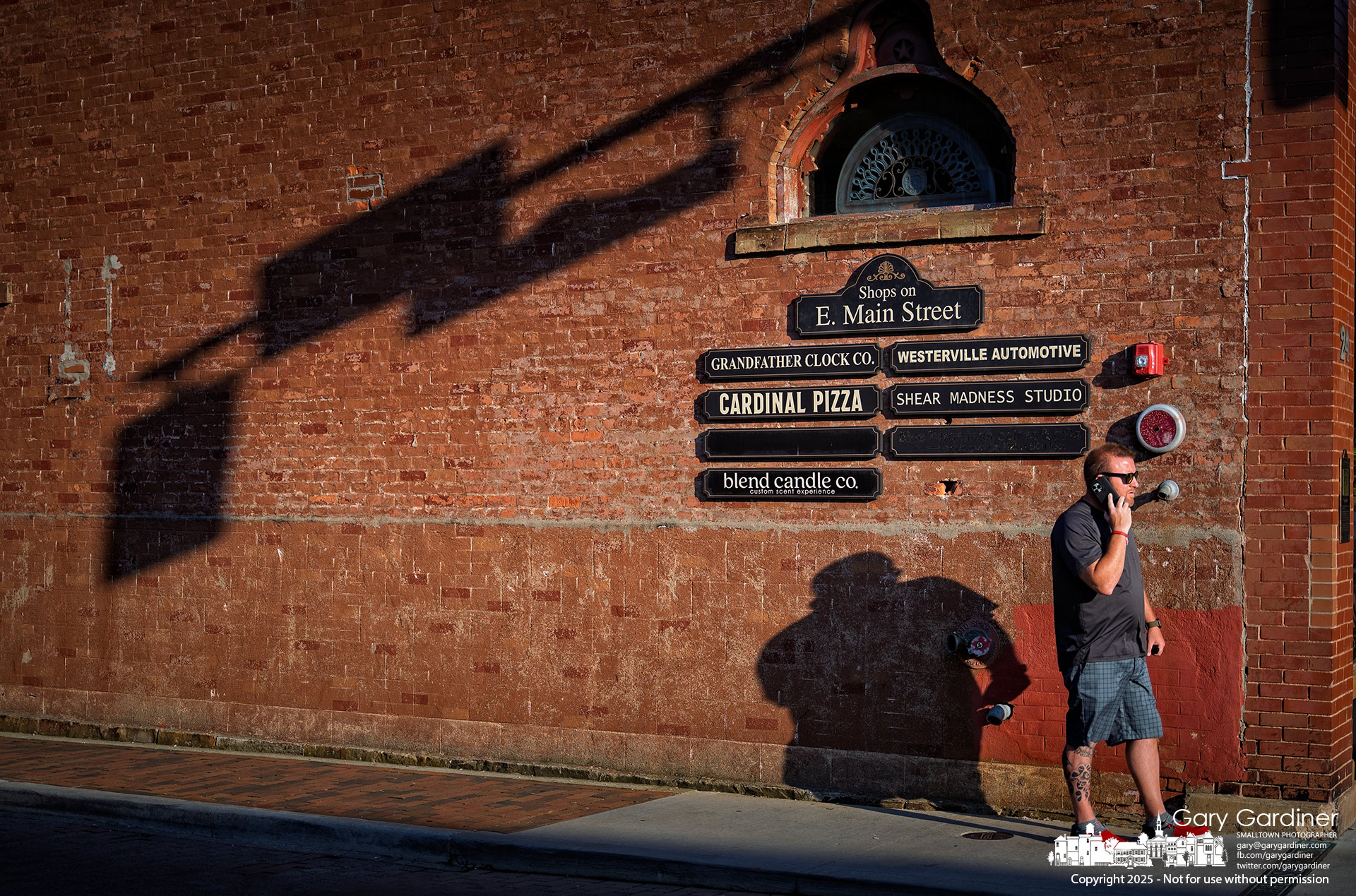 A man talks on his phone as the setting sun casts long shadows across the brick storefronts on East Main Street in Uptown Westerville on Friday evening. My Final Photo for July 11, 2025.