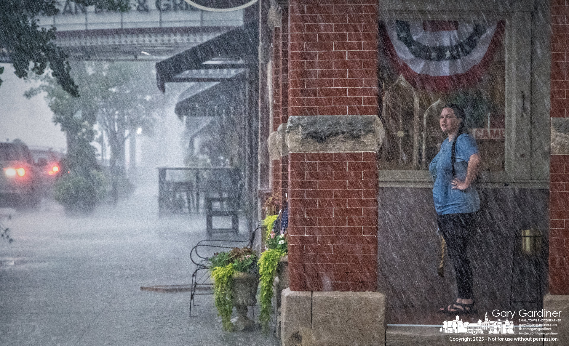 A woman, already soaked by a sudden afternoon downpour, takes shelter in the portico at Westerville Antiques as she waits for the rain to ease before continuing her journey. My Final Photo for July 16, 2025.