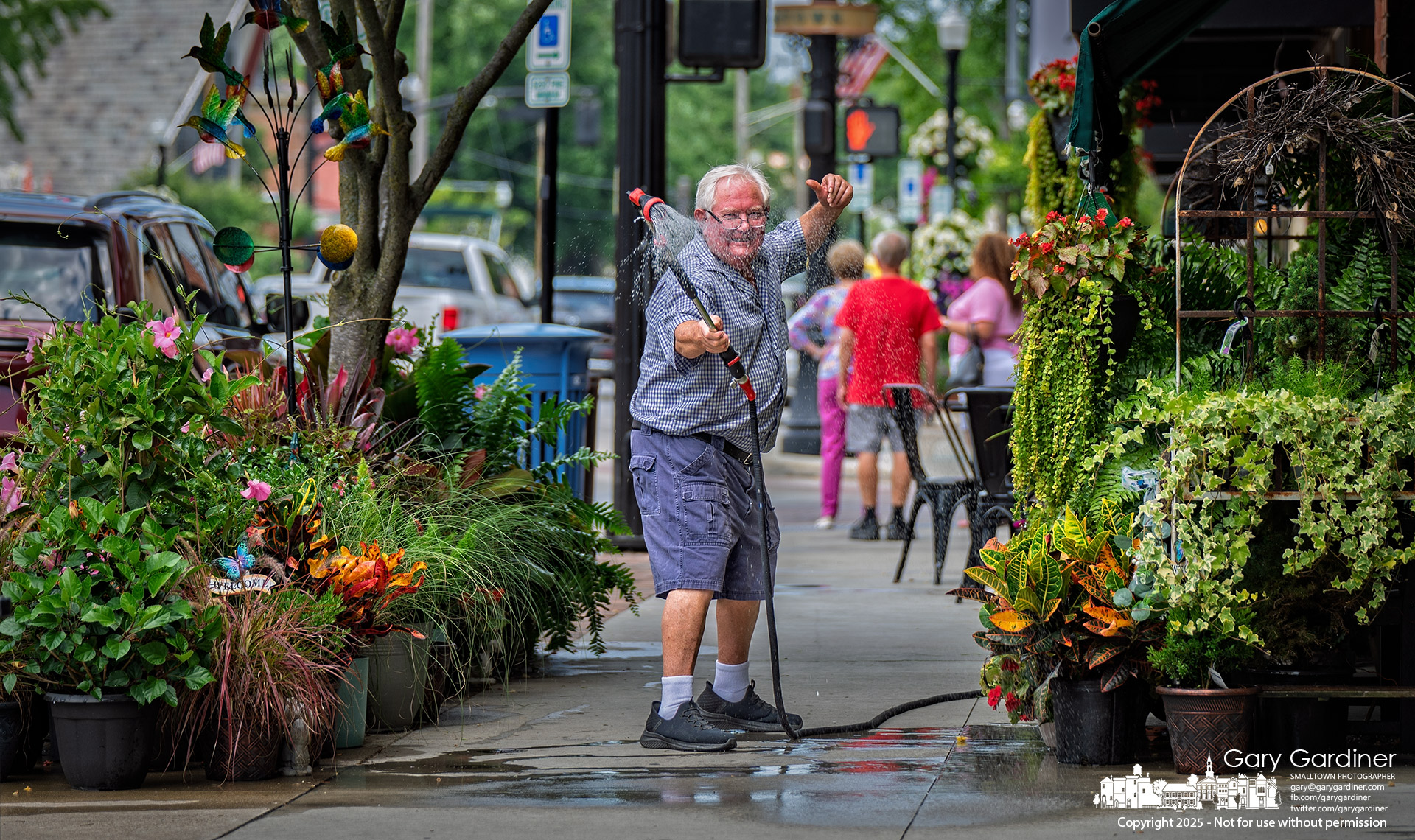 Florist Dave Talbott strikes an en garde pose with his gardening hose, playfully guarding the colorful sidewalk garden outside his Uptown shop. My Final Photo for August 5, 2025.