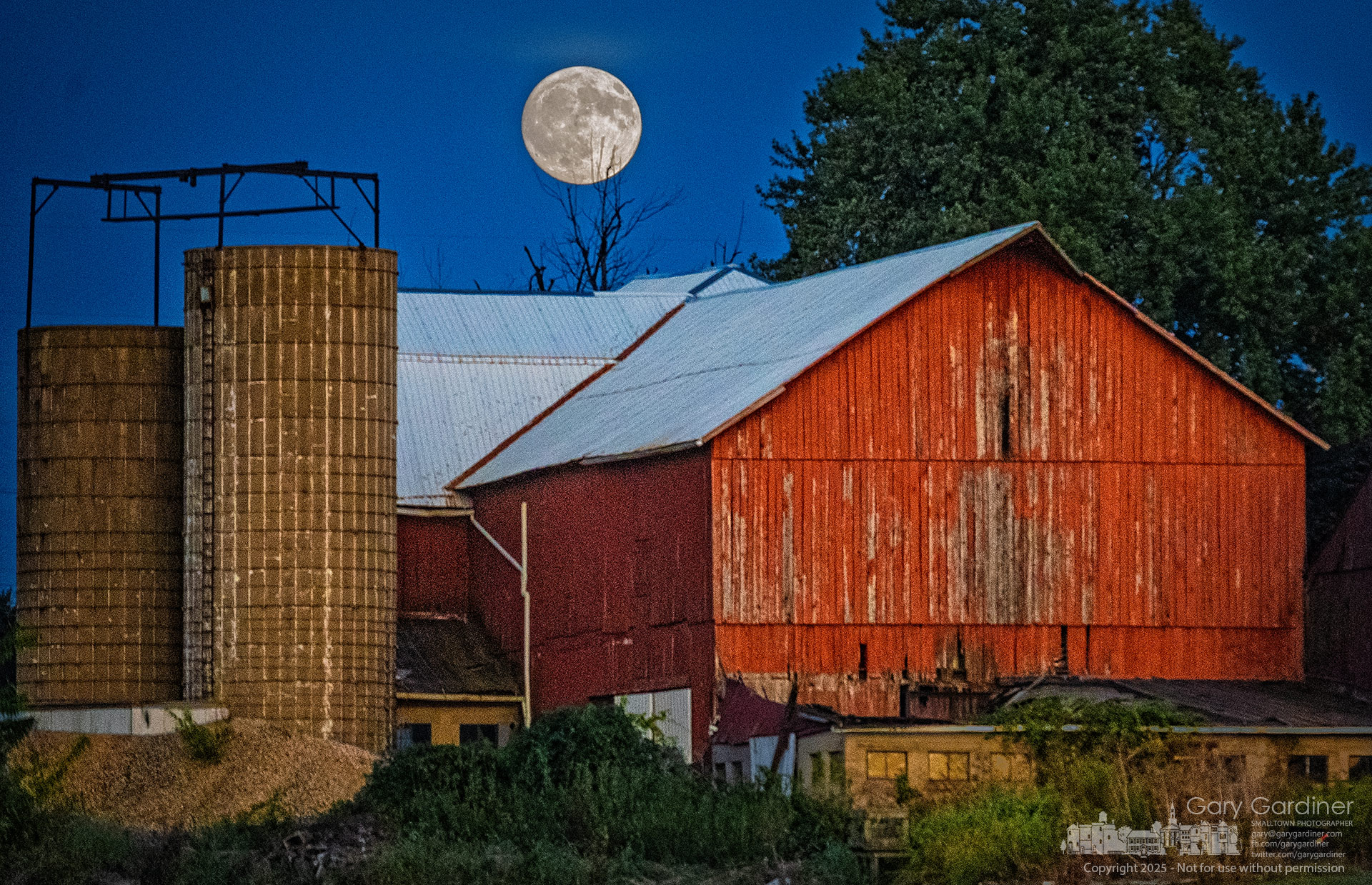 A full moon rises behind the weathered red barn and silos at the Yarnell Farm on a late-summer evening, casting a serene glow over the historic farm. My Final Photo for September 6, 2025.