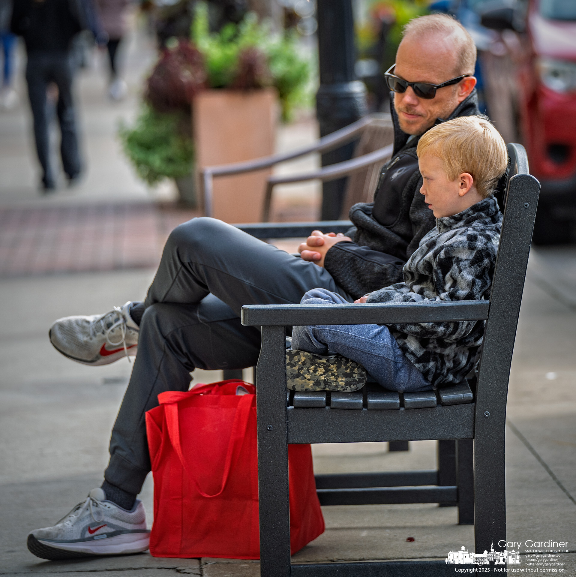 A father advises his son on the proper method to sit quietly on a sidewalk bench while his mother and sister shop at Cinda Lou's in Uptown Westerville. My Final Photo for October 25, 2025.