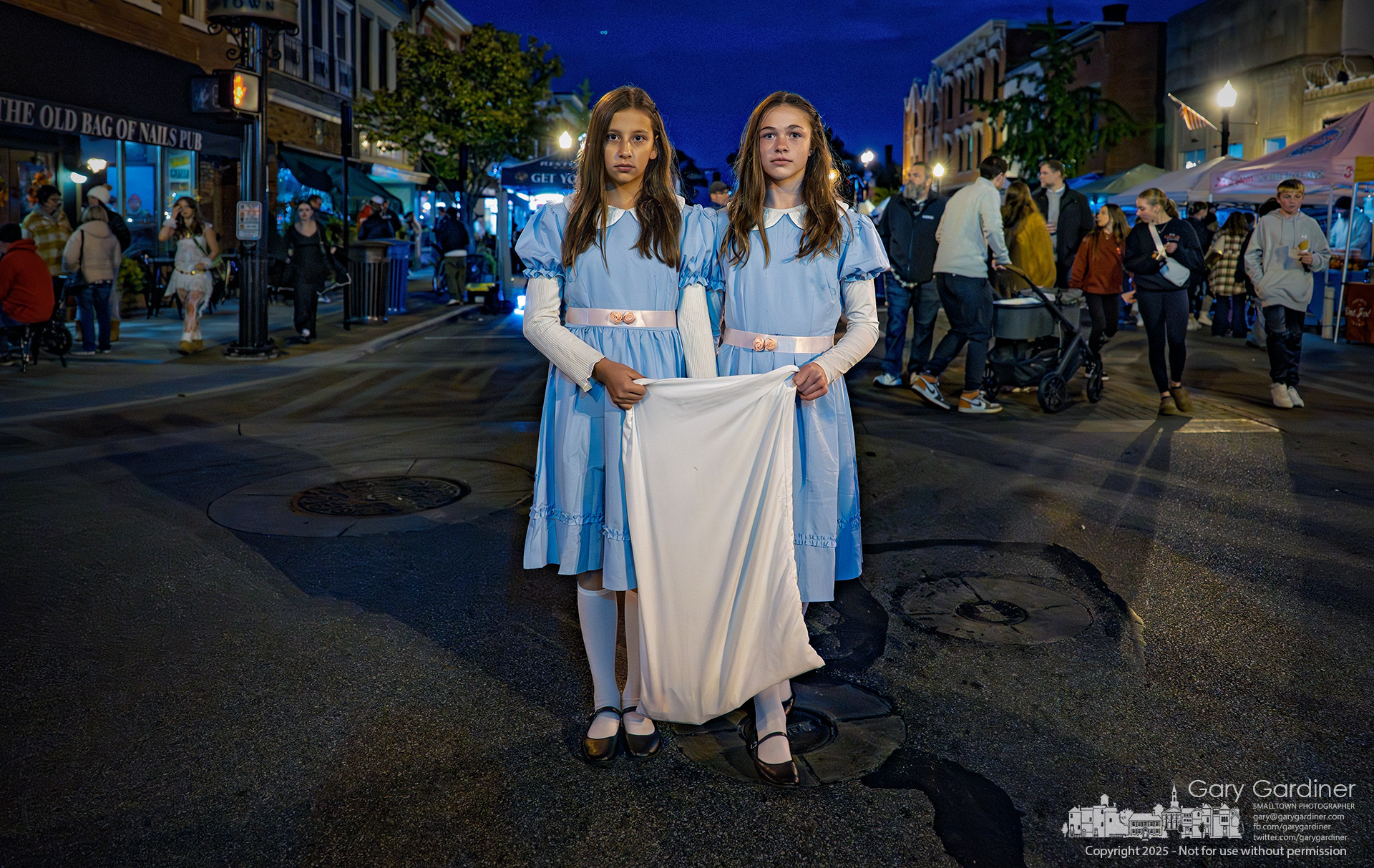 Dressed as the eerie twins from The Shining, two girls silently walked through Midnight Madness Fourth Friday while holding a Halloween pillowcase to collect candy or donations with unsettling calm. My Final Photo for October 24, 2025.