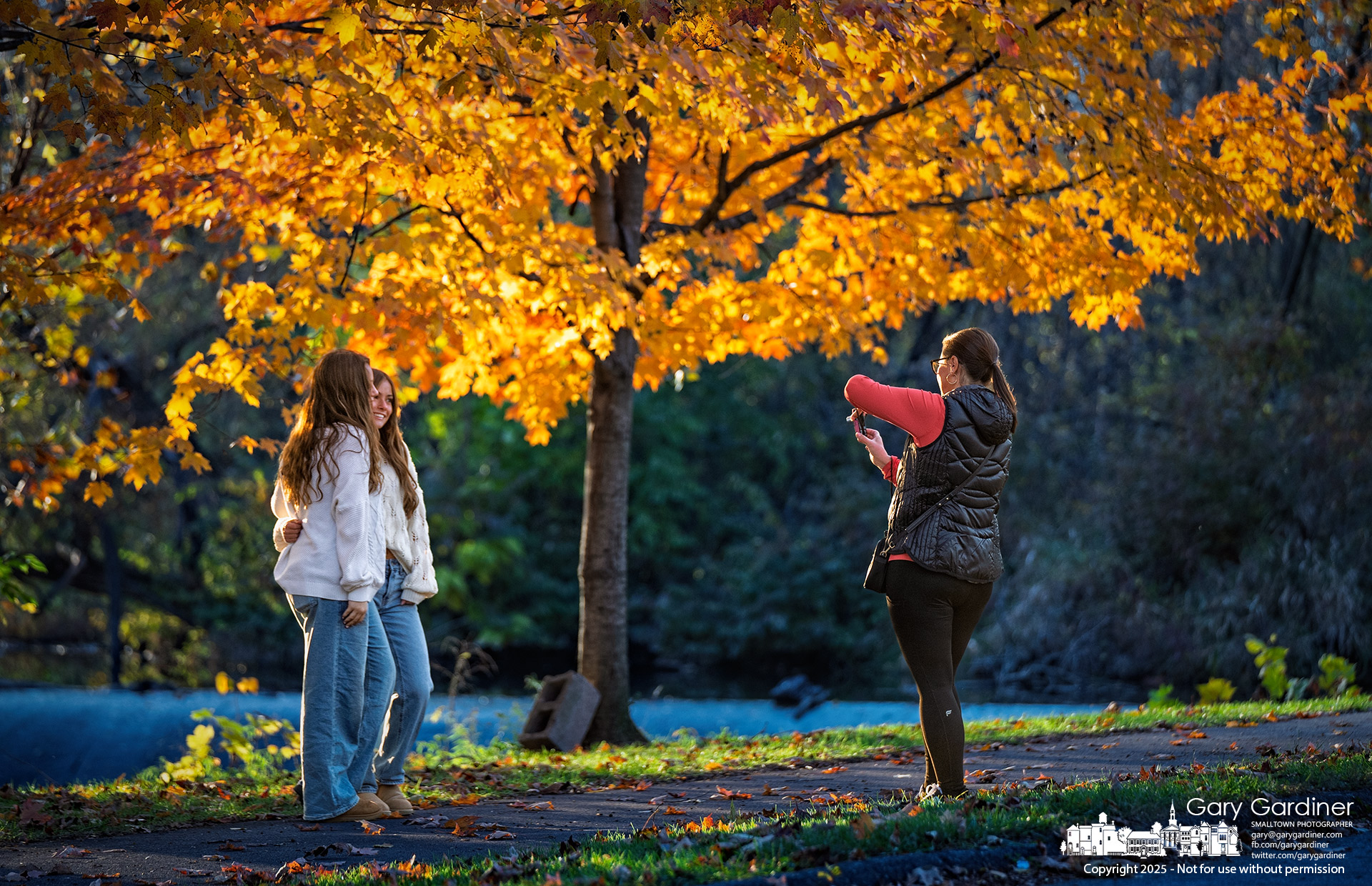 Best friends pose for a photo taken with a point-and-shoot digital camera by the mother of one of them, framed by the golden colors of fall at the Alum Creek Park North Dam. My Final Photo for November 2, 2025.