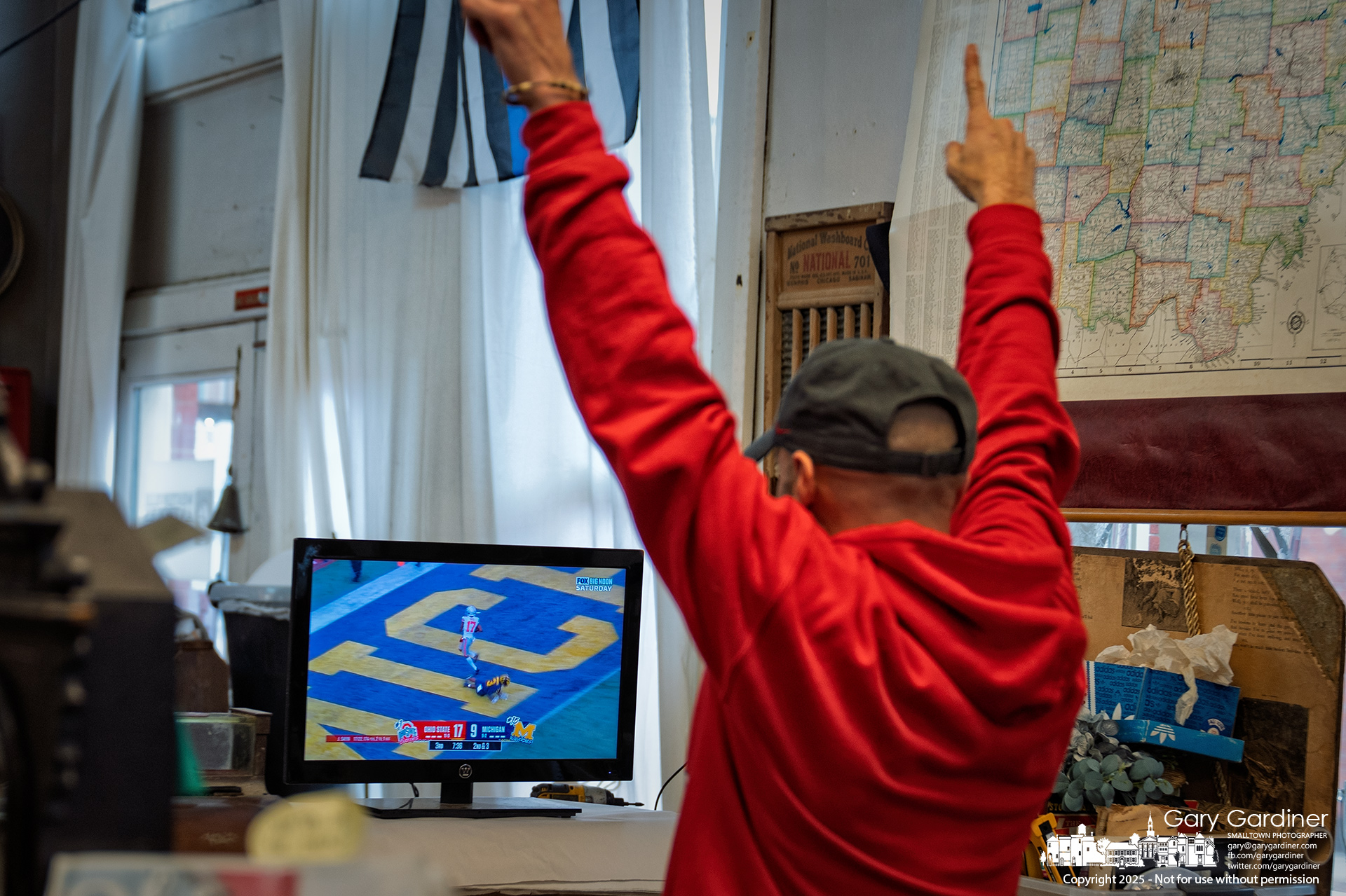 Luke Ernst, owner of Westerville Antiques, cheers as Ohio State scores against Michigan while watching the game from behind the counter of his Uptown store, one of many working on OSU-Michigan Saturday. My Final Photo for November 29, 2025.