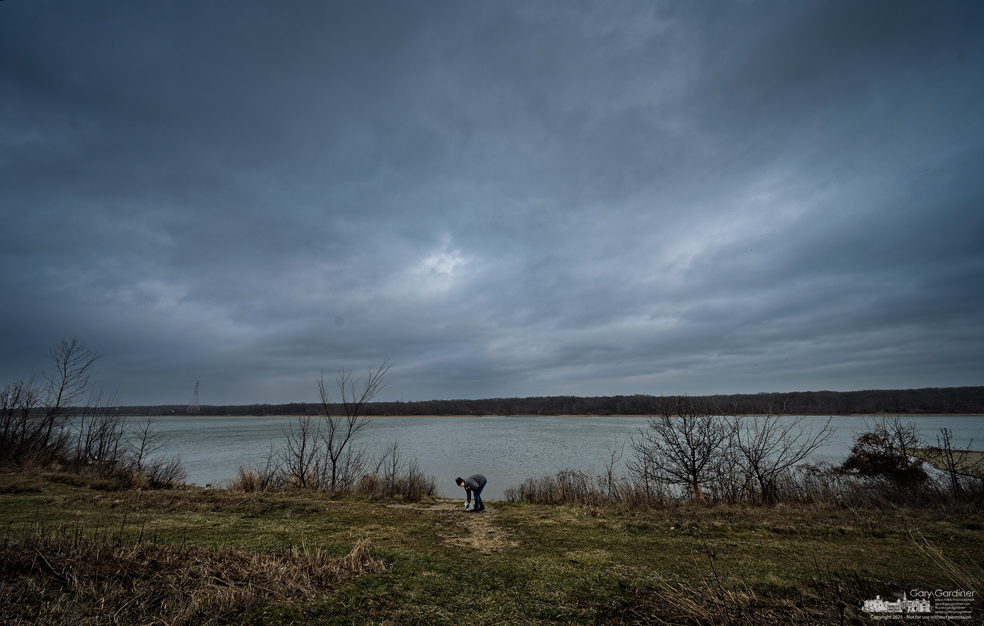 A woman searches the shoreline of Hoover Reservoir, collecting rocks after failing to find the ring she lost over the weekend. My Final Photo for December 29, 2025.