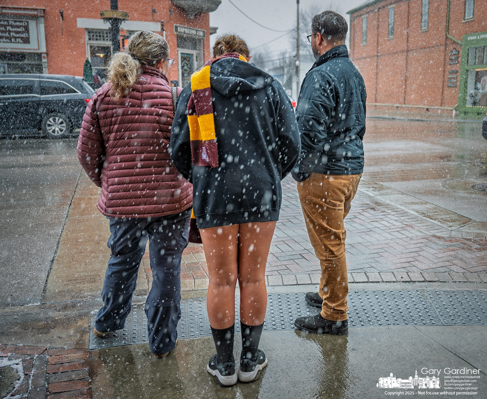 Parents and their teenage daughter, dressed for a warmer indoor activity, stand ready to cross State Street as the first snow begins to fall in Uptown. My Final Photo for December 13, 2025.