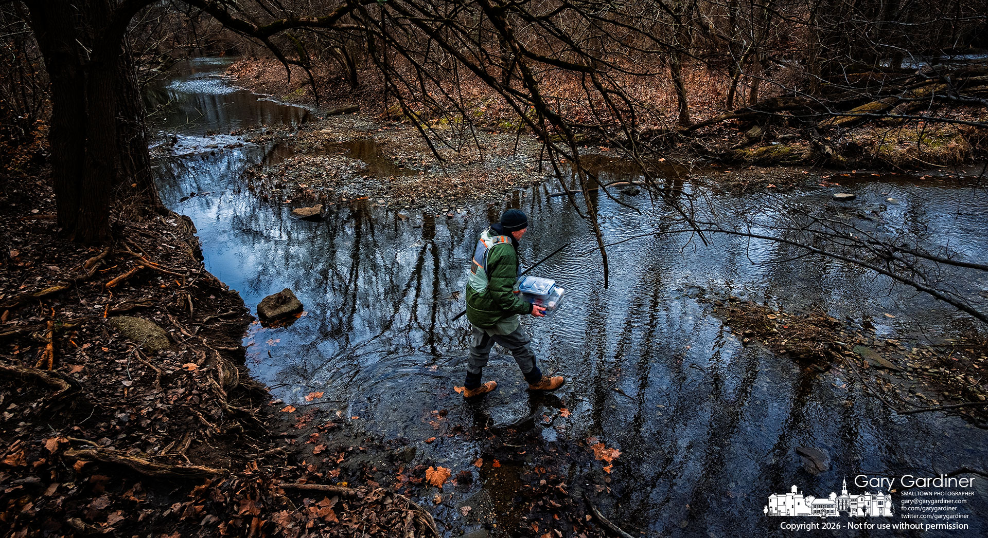 A fisherman wades into the shallows below the Alum Creek Dam in Westerville, carrying his tackle boxes as the blue shadows of late afternoon begin to darken the creek. My Final Photo for January 9, 2026.