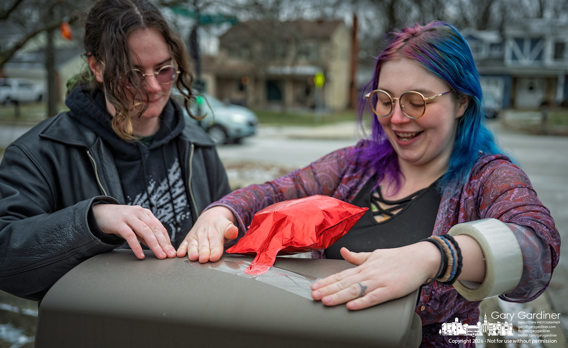 Four-year-old Nora’s mother, at right, and her sister tape inflated stars to trees, a street sign, and the mailbox to help guests find the party later Saturday. My Final Photo for January 16, 2026.