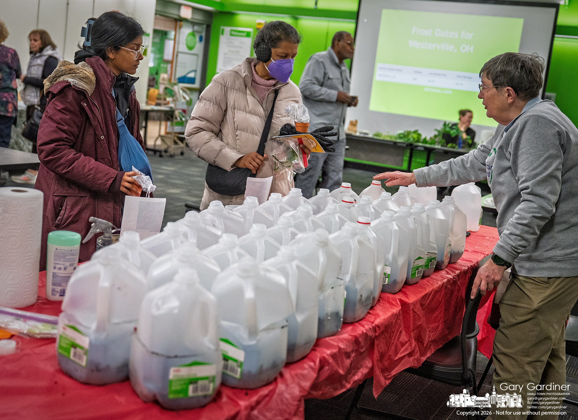 Volunteers explain how to care for plastic gallon-jug greenhouses as gardeners pick them up Saturday at the Seed and Plant Swap at the library.