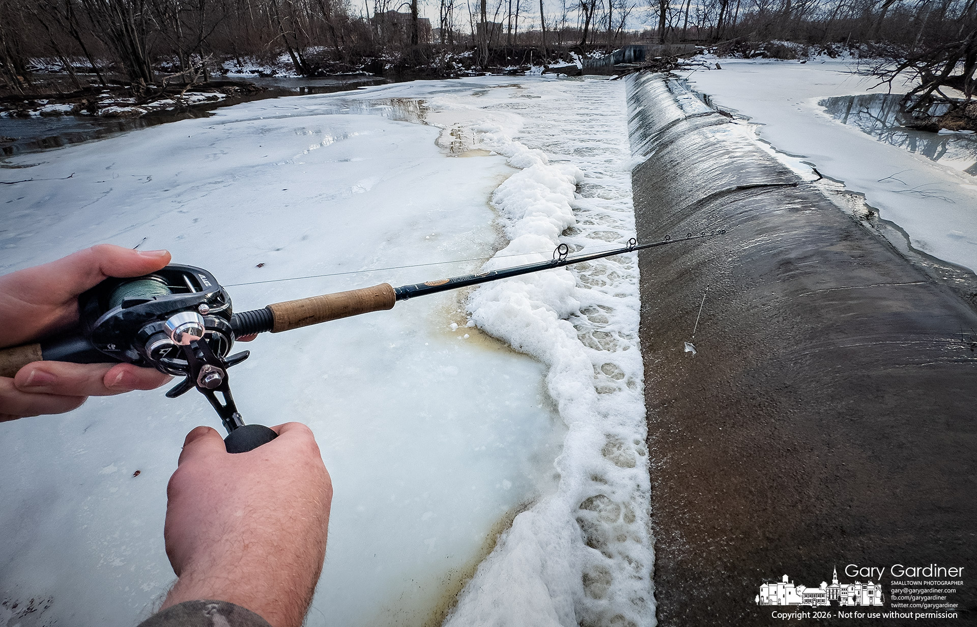 A fisherman retrieves his lure from the narrow strip of open water between the dam and ice at Creek Park North Dam as warm weather melts the heavy snowfall and thaws the river. (My Final Photo for February 15, 2026)