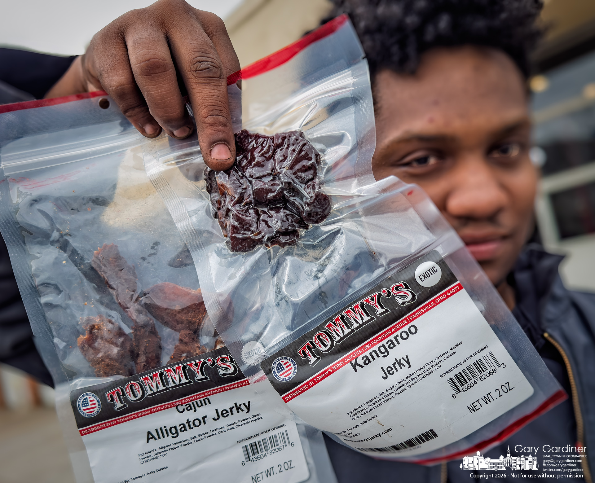 A mechanic holds bags of alligator and kangaroo jerky he bought for a snack from Tommy's Jerky truck that stopped at his garage Monday afternoon. (My Final Photo for March 23, 2026)