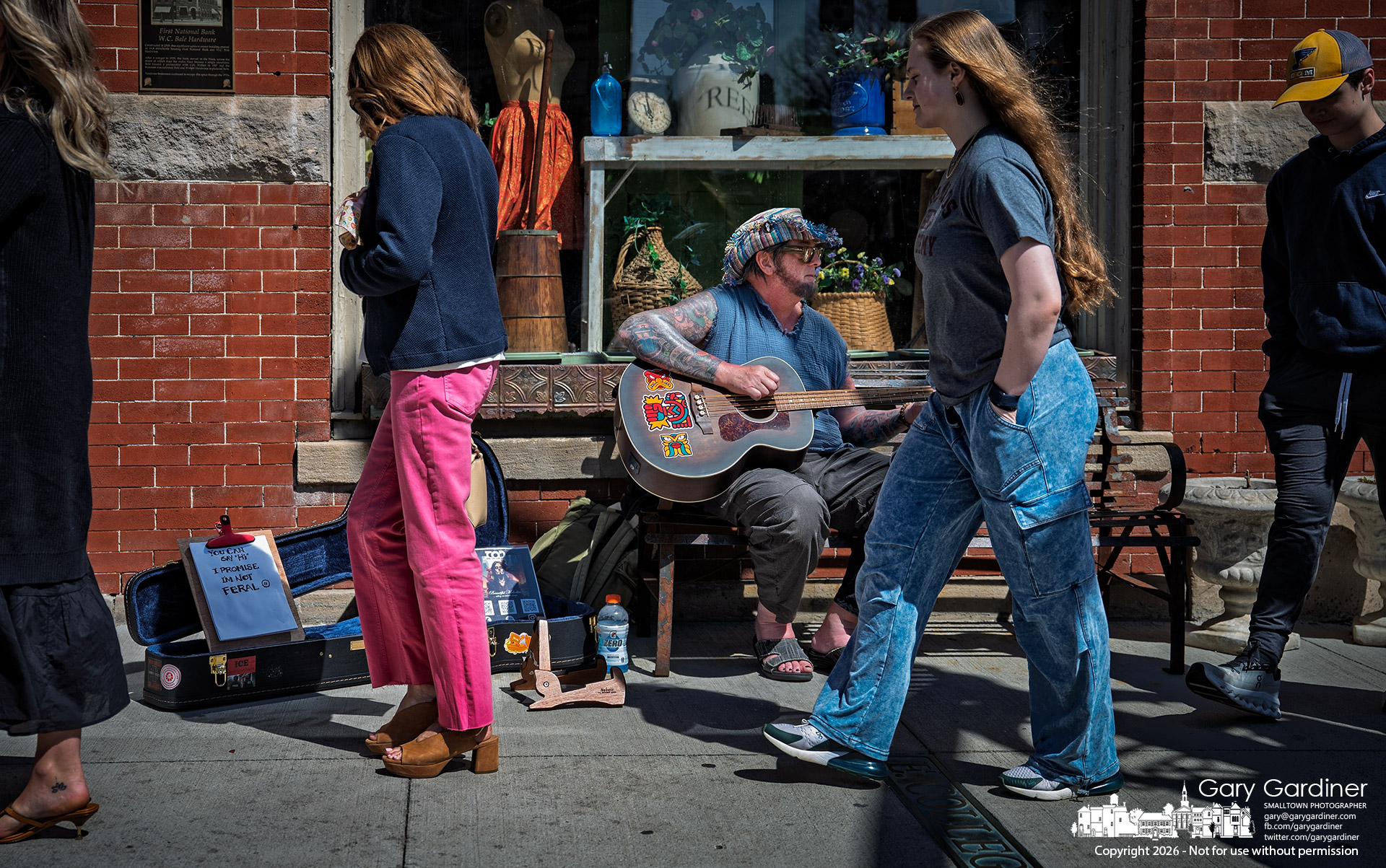 A busker plays from the bench in front of Westerville Antiques, where a steady flow of listeners passed by on a warm spring afternoon. (My Final Photo for April 11, 2026)
