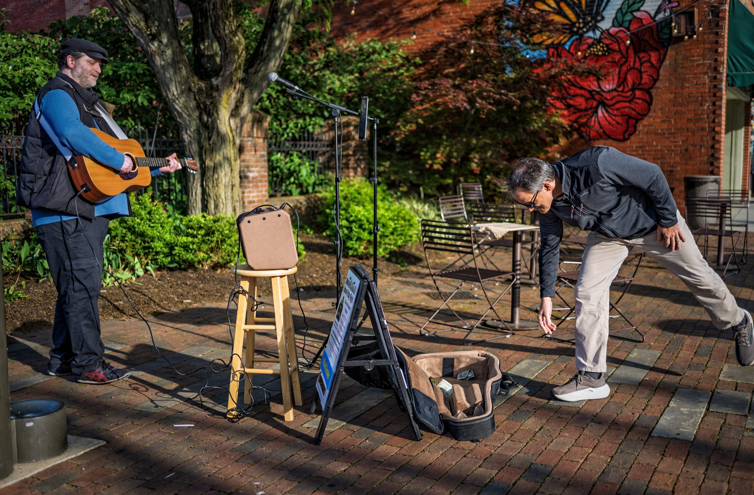 A passing fan tosses cash into the guitar case of Mark Zonakis performing at Rotary Park on the first night of musicians at Uptown Friday Night. My Final Photo for May 1, 2026, by Gary Gardiner)