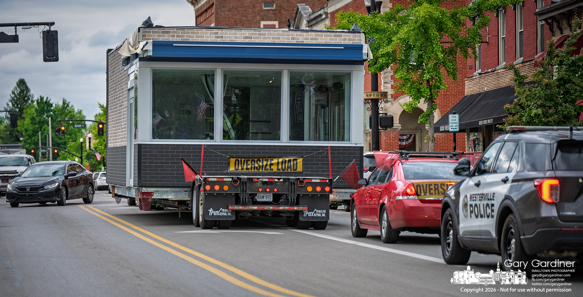 An oversized load that appears to be a food-service kiosk travels through Uptown Wednesday evening to a destination north of Westerville. (My Final Photo for May 13, 2026. Photo by Gary Gardiner)