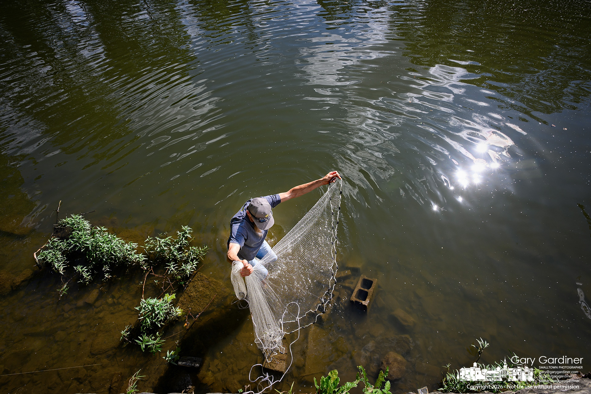 Angler Chad retrieves his casting net from the rocks and blocks that caught it in the shallows below the Alum Creek Dam as he was casting for baitfish. (My Final Photo for June 18, 2026. Photo by Gary Gardiner)