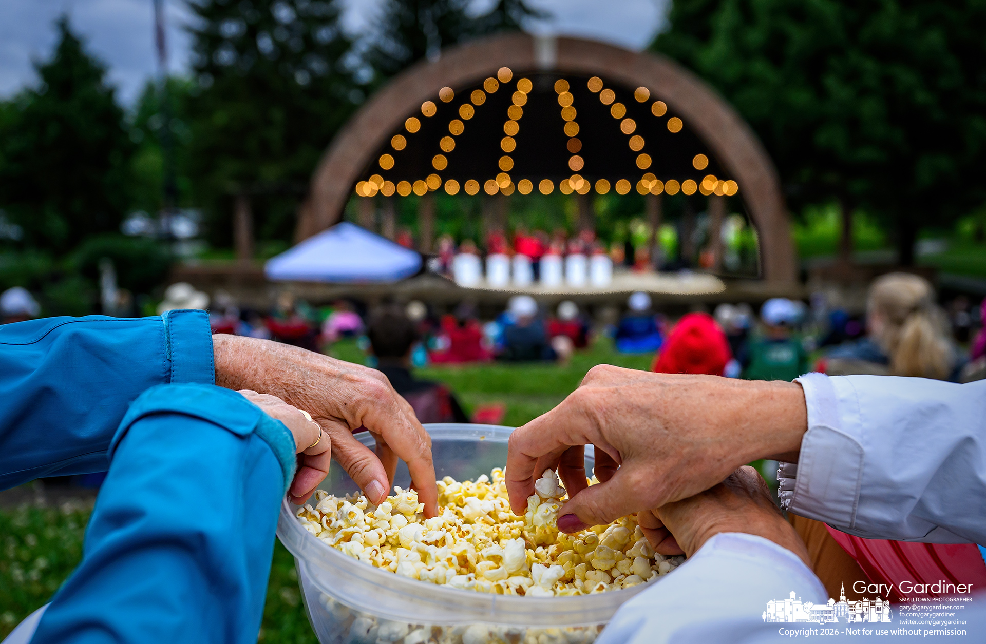 Concertgoers share a container of popcorn they brought to the Westerville Jazz Orchestra's performance, as weather conditions ranged from sprinkling rain to a bright sunset. (My Final Photo for June 14, 2026. Photo by Gary Gardiner)
