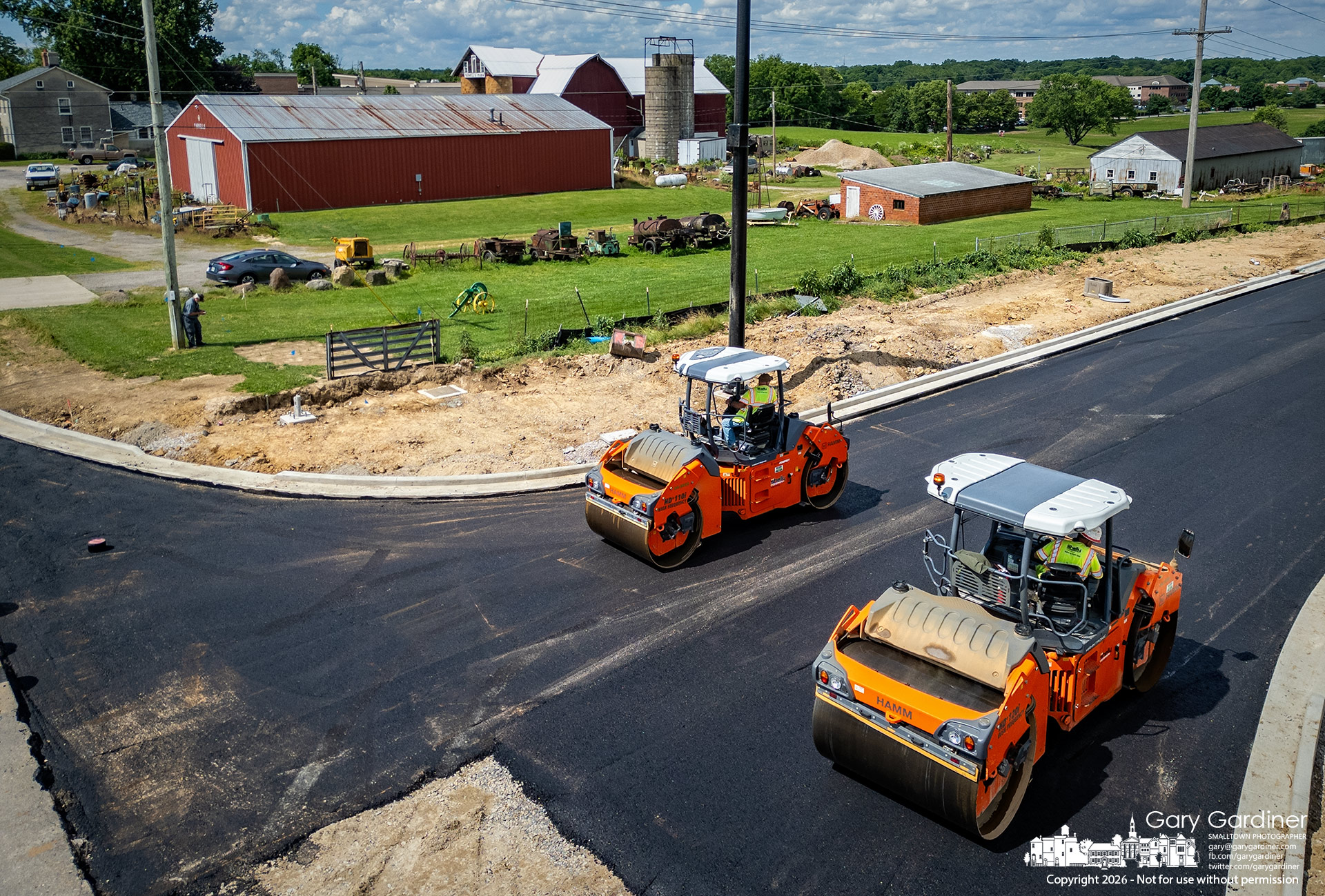 Steamrollers flatten sections of the new Westar Boulevard roadway laid Tuesday beside the barns and buildings at the Yarnell Farm. (My Final Photo for June 16, 2026. Photo by Gary Gardiner)