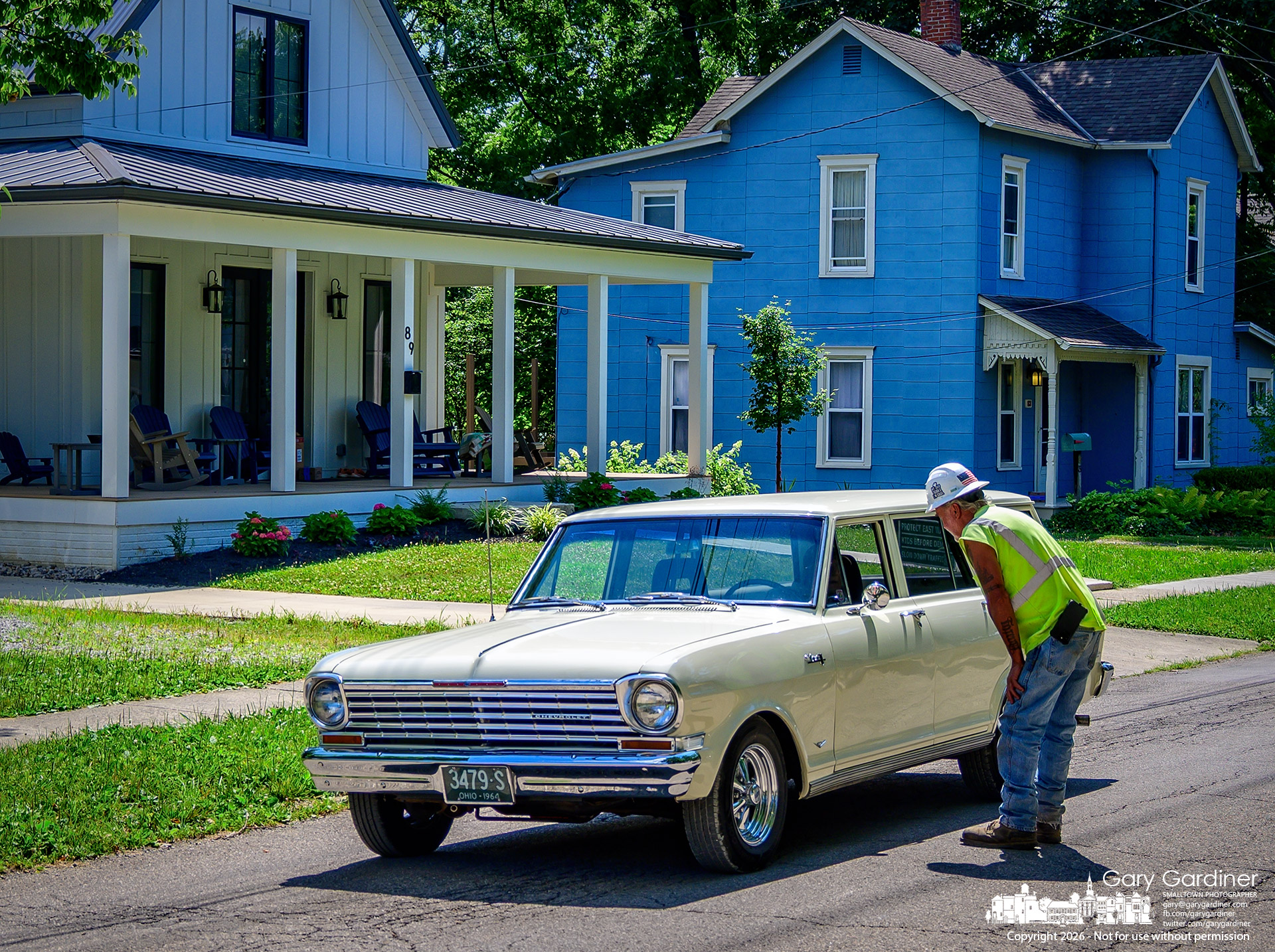 A construction worker talks with the driver of a 1964 Chevrolet Chevy II Nova station wagon after the vehicle stopped on East Park Street while equipment was moved from the bike trail renovation. (My Final Photo for July 8, 2026. Photo by Gary Gardiner)