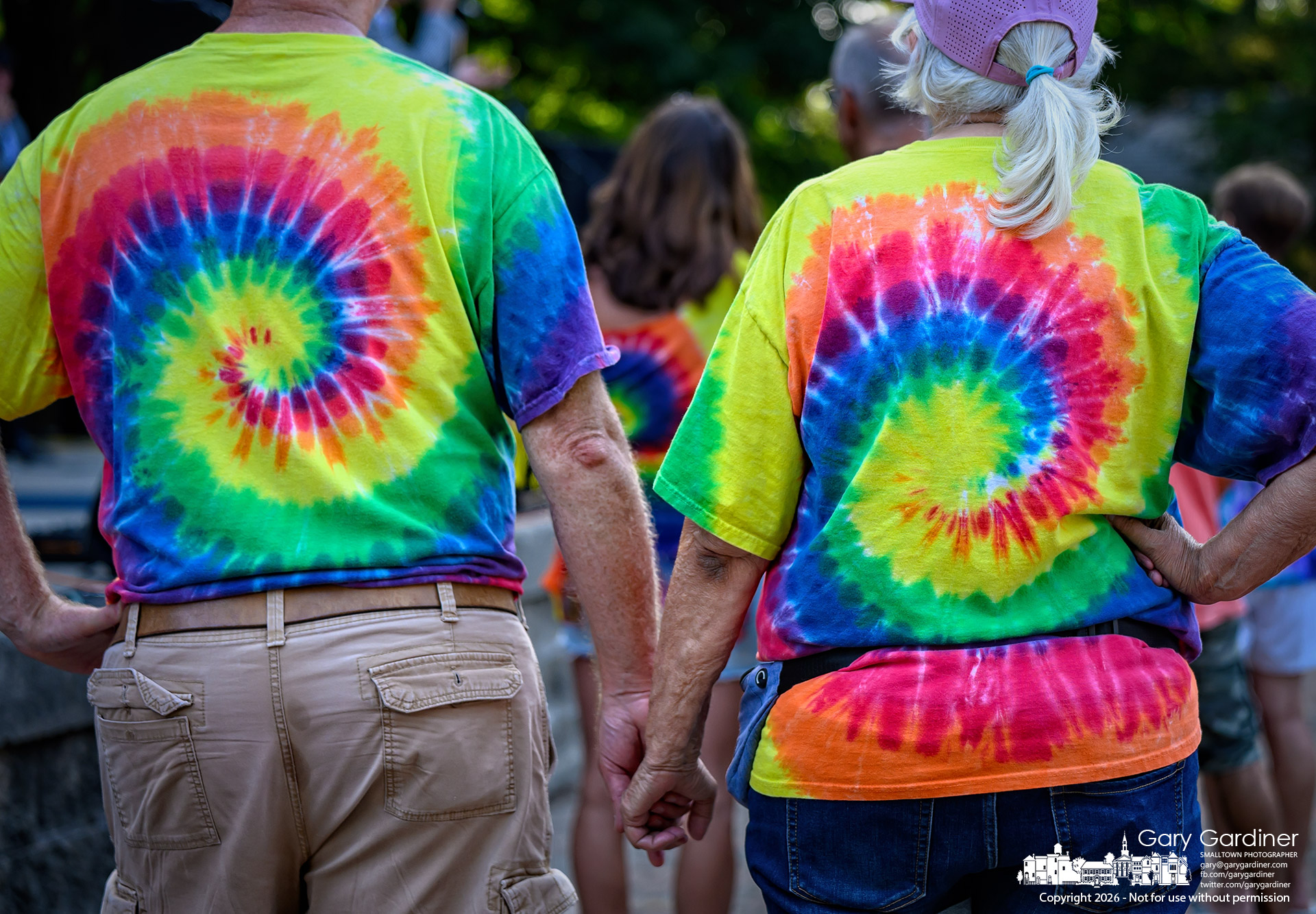 A couple wearing British Invasion tie-dye shorts holds hands during a pause in the group's concert in the Alum Creek Amphitheater Sunday night. (My Final Photo for July 19, 2026)