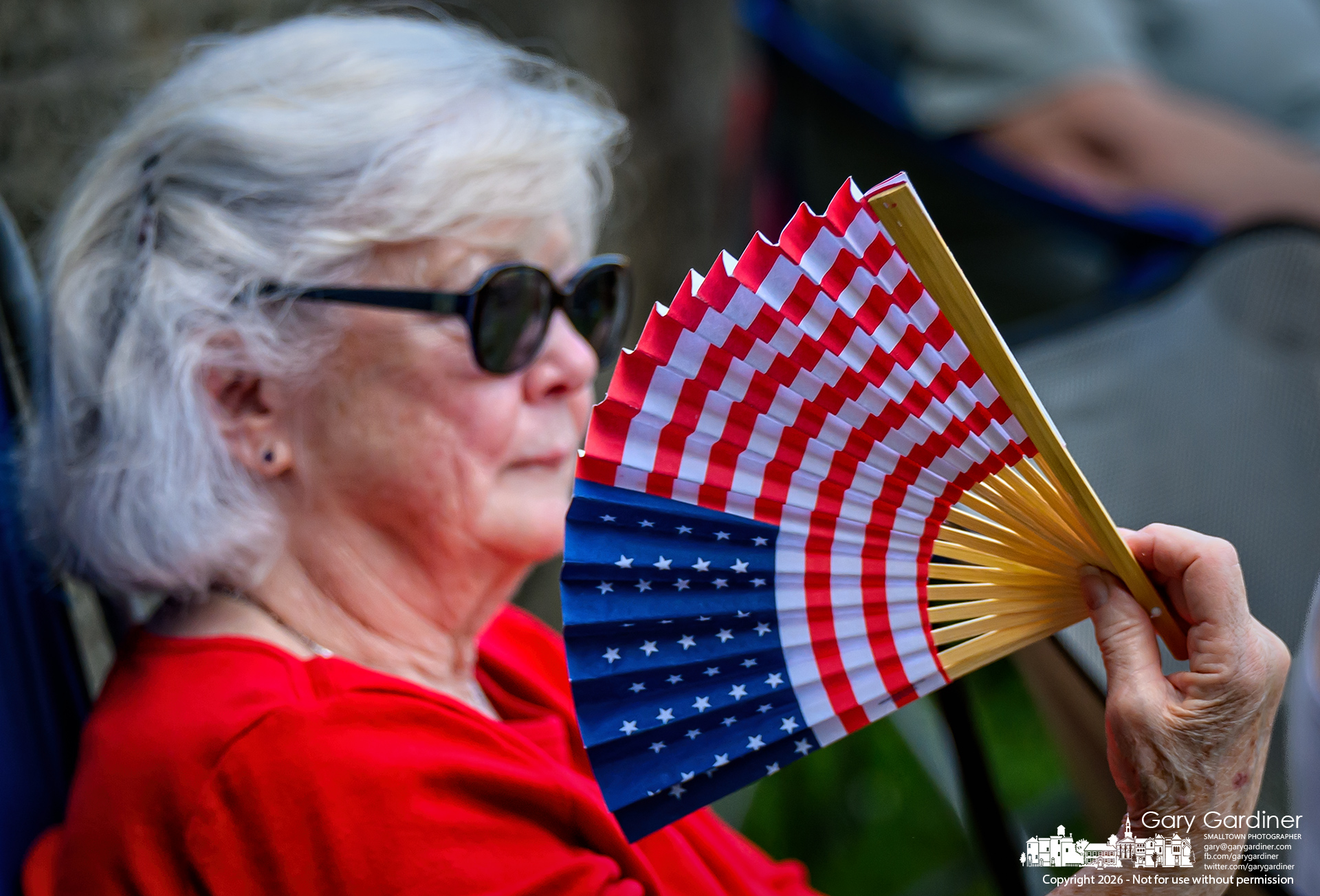A woman cools herself with a patriotic fan during the Westerville Concert Band's performance Sunday night at the Alum Creek Park Amphitheater. (My Final Photo for July 5, 2026. Photo by Gary Gardiner)
