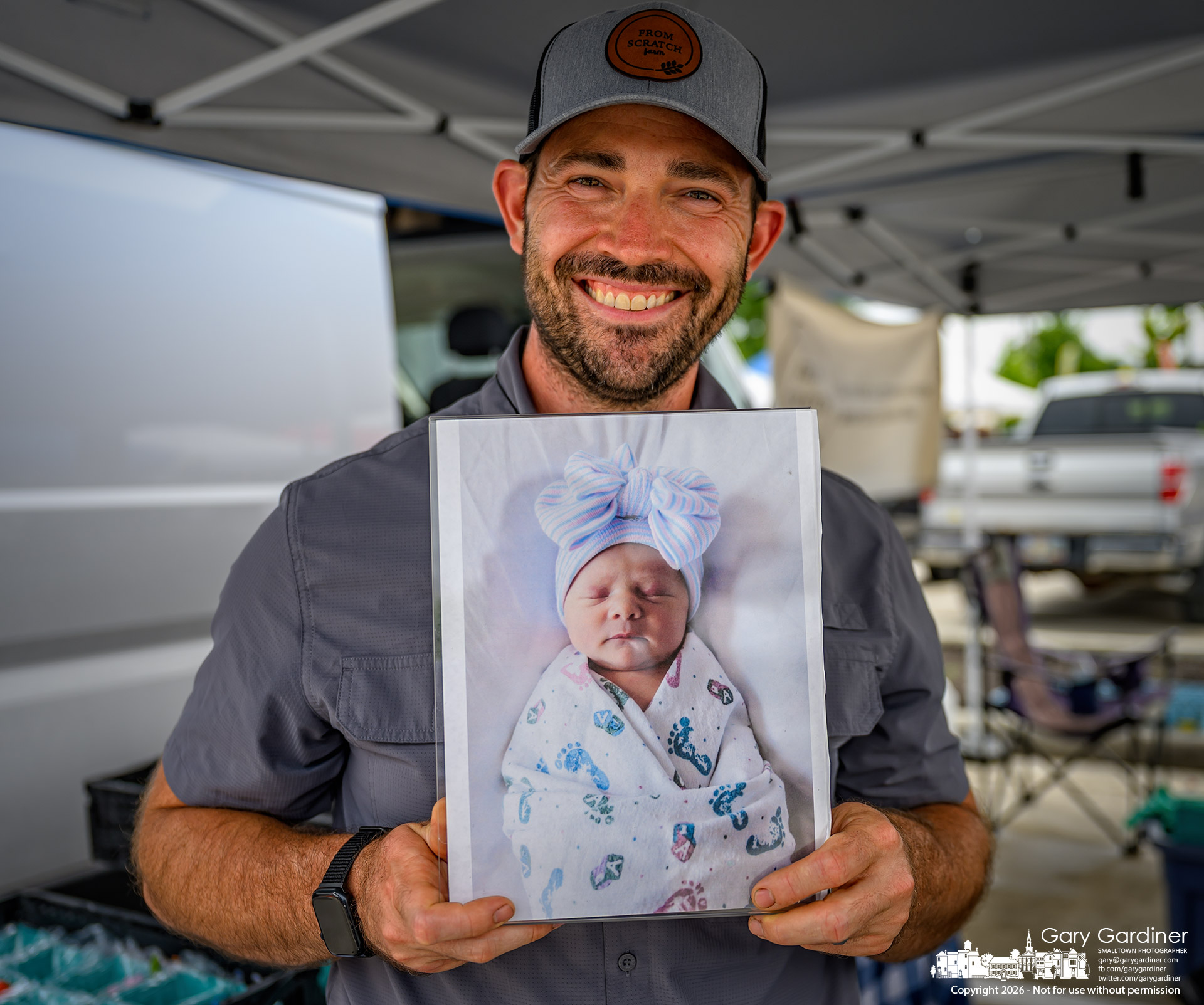 Johnstown farmer and Westerville Saturday Farmers Market vendor proudly shows off a photo of Madelyne May, his newborn daughter. (My Final Photo for July 11, 2026. Photo by Gary Gardiner)
