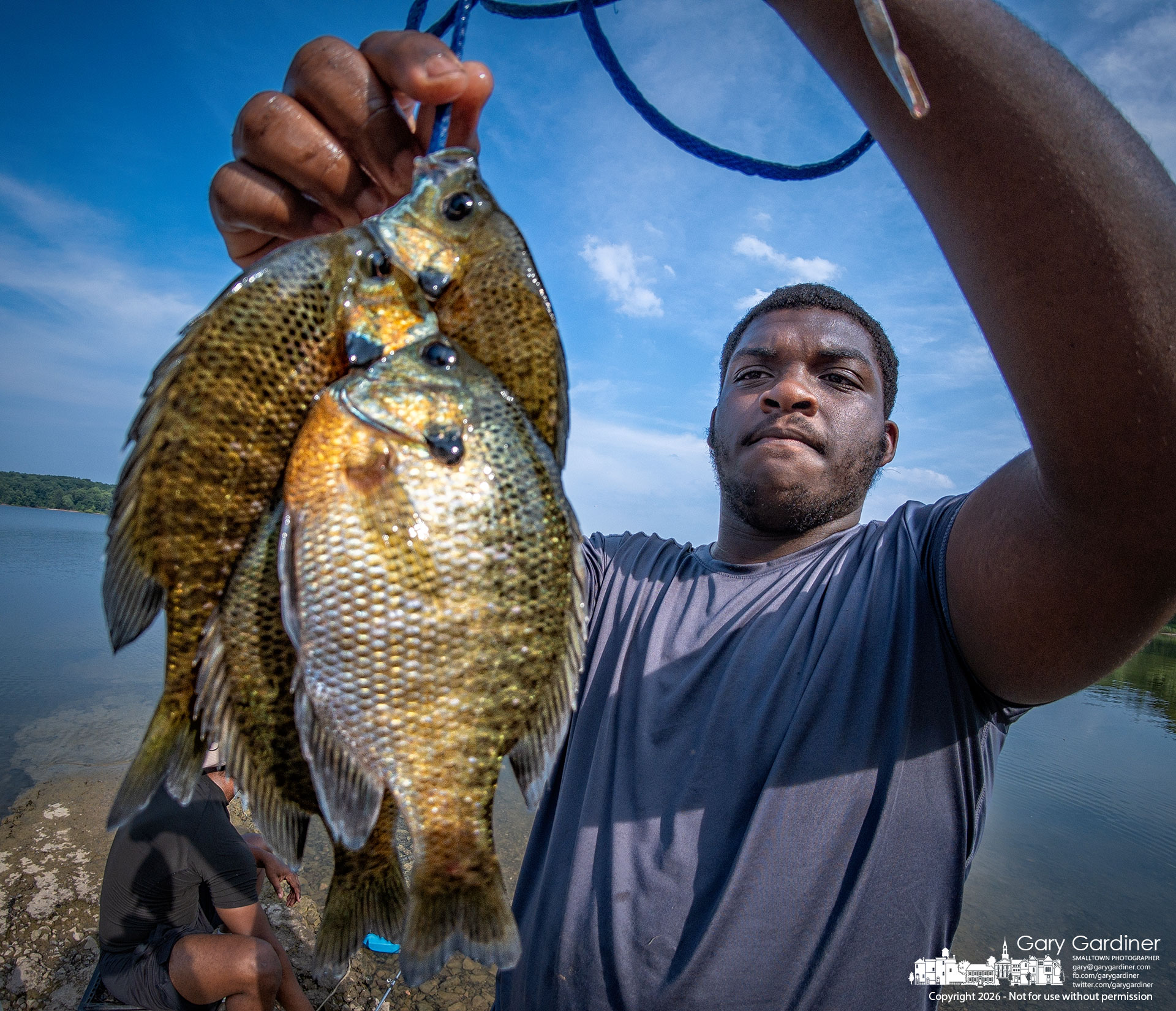 A fisherman proudly displays the string of bluegill he caught at the end of Walnut Street before it disappears beneath Hoover Reservoir. (My Final Photo for July 20, 2026. Photo by Gary Gardiner)