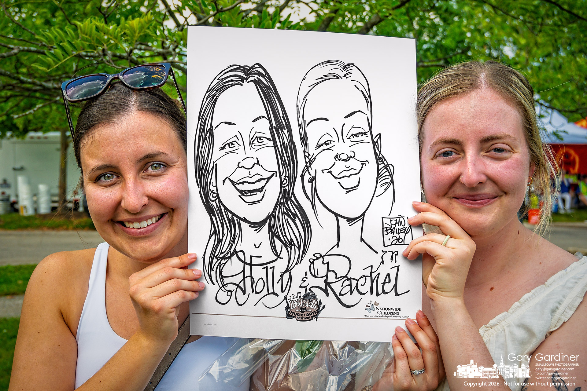 Twin sisters Holly and Rachel show the caricature made of them during the last few minutes of the Westerville Music and Arts Festival Sunday. (My Final Photo for July 12. Photo by Gary Gsardiner)