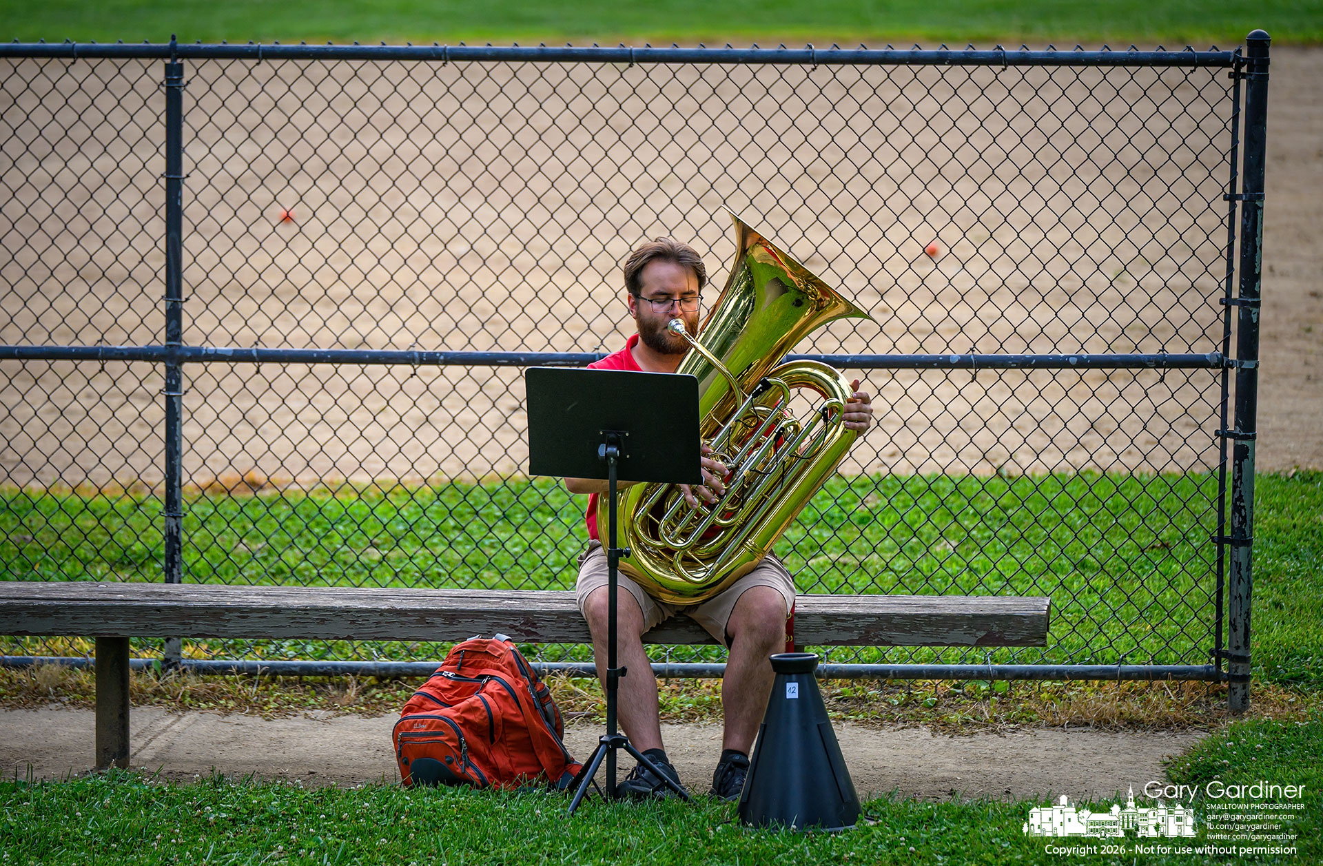 Ethan Morris practices from the home-team dugout before playing tuba with the Westerville Concert Orchestra at the Sunday concert series in the amphitheater in Alum Creek Park North. (My Final Photo for July 26, 2026. Photo by Gary Gardiner)