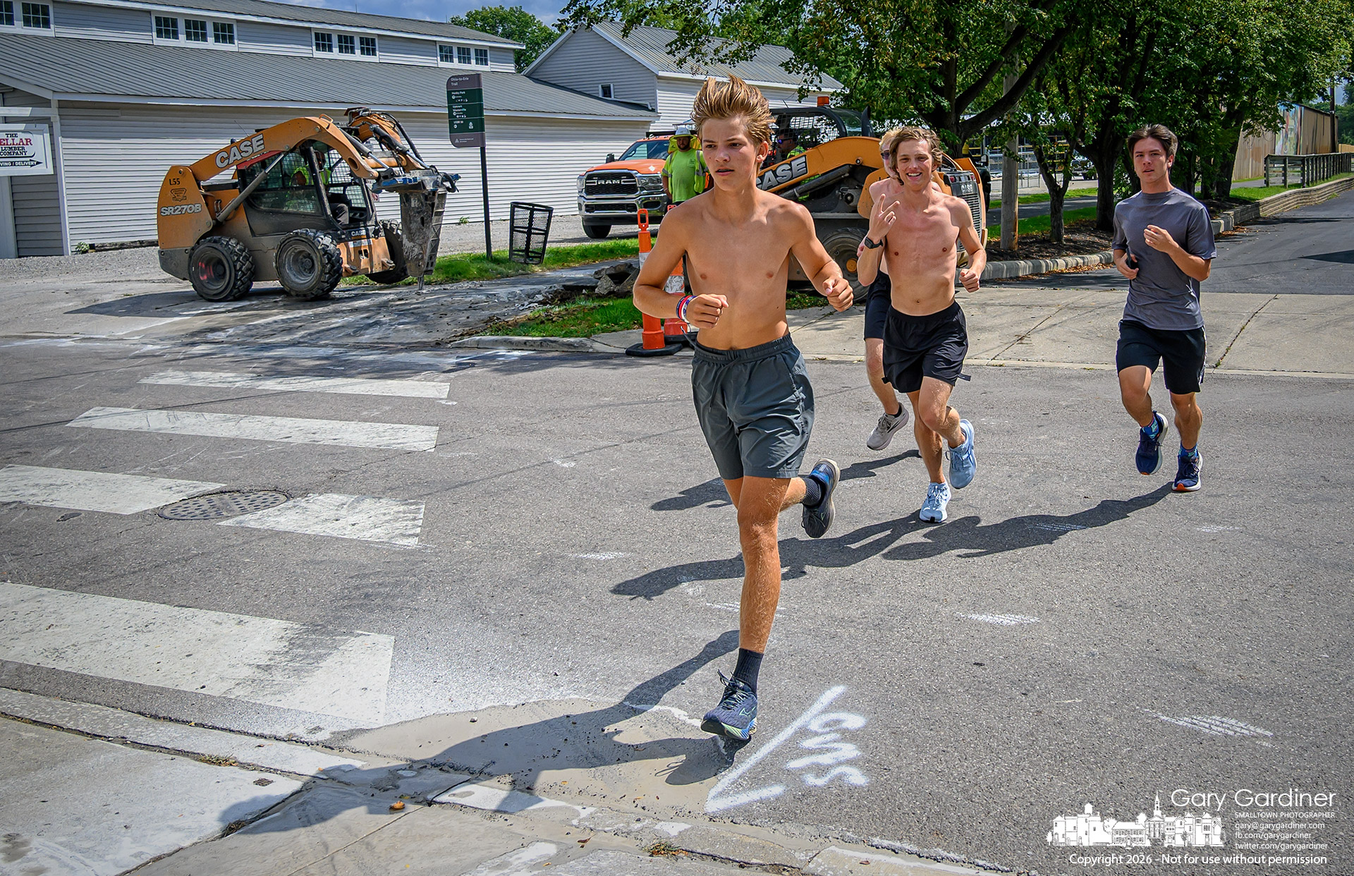 Runners bypass the marked East College Ohio Trail crossing, avoiding construction equipment removing old concrete and asphalt at the junction of the trail and the roadway. (My Final Photo for August 24, 2026. Photo by Gary Gardiner)