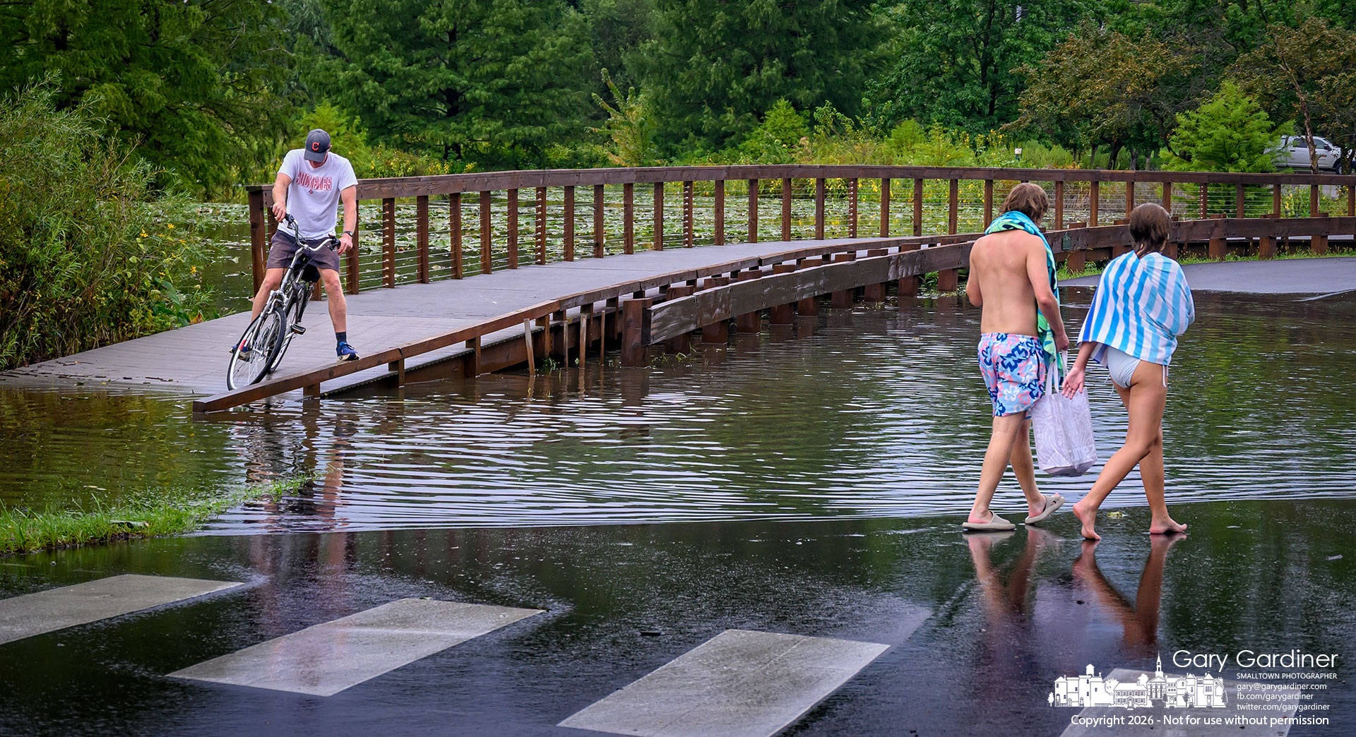 Portions of the bike path and the roadway were underwater Monday after heavy rains filled holding ponds and runoff streams, causing temporary blockages at Highlands Park. (My Final Photo for August 17, 2026. Photo by Gary Gardiner)