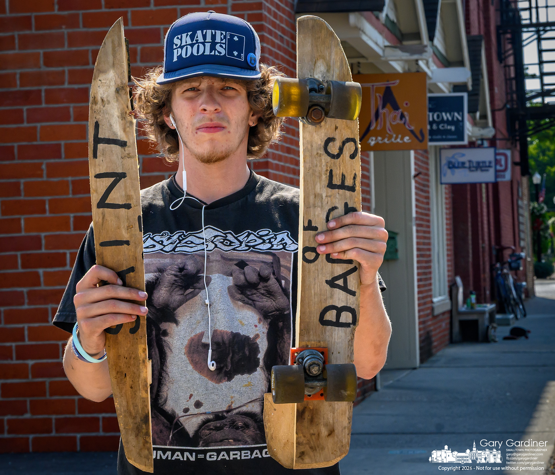 A skateboarder holds his broken board after running into a curb, snapping the vintage wooden board along the grain. (My Final Photo for August 6, 2026. Photo by Gary Gardiner)