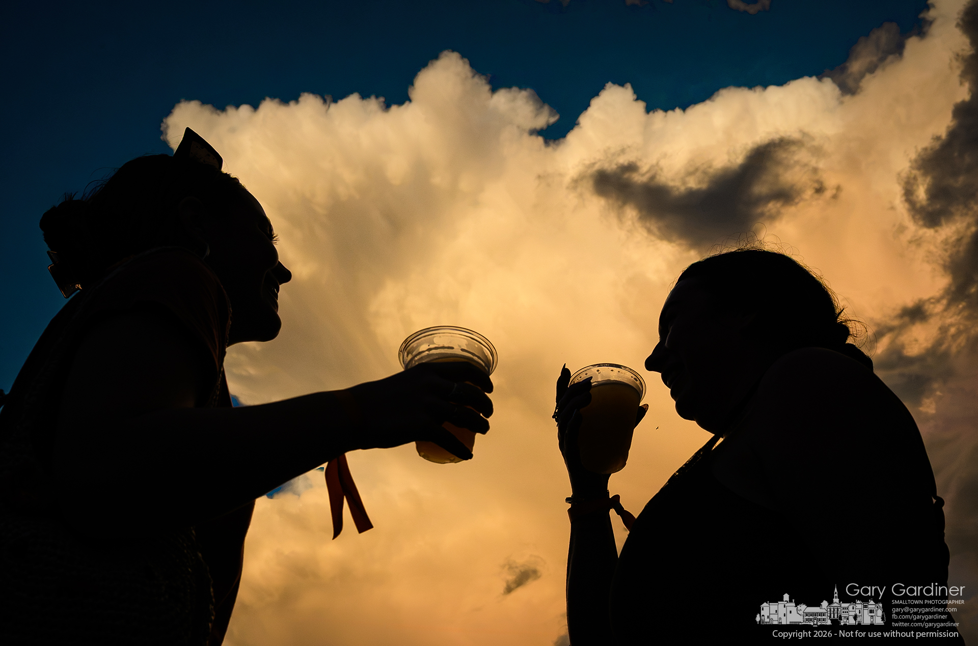A passing storm cloud is brightened by the setting sun after drenching Uptown Untapped, where these two women stood their ground against the weather and continued enjoying each other's conversation and the remaining crowd's undampened enthusiasm. (My Final Photo for August 8, 2026. Photo by Gary Gardiner)