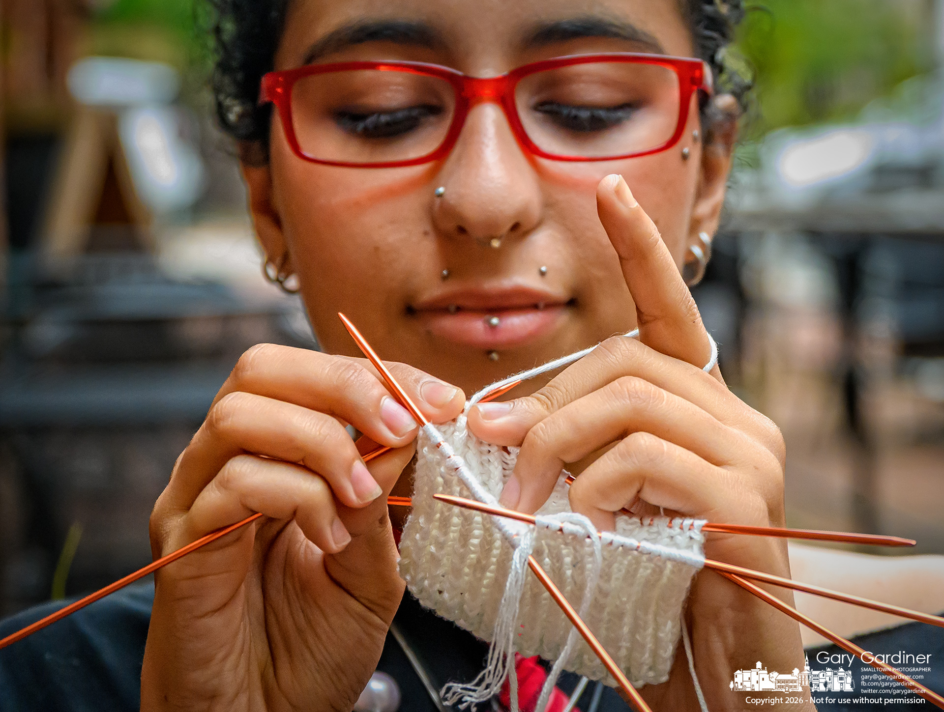 Yaz Kassab studies her next stitch as she knits herself the first of a pair of socks during a quiet time on the brick next to Java Central in Uptown. (My Final Photo for August 19, 2026. Photo by Gary Gardiner)
