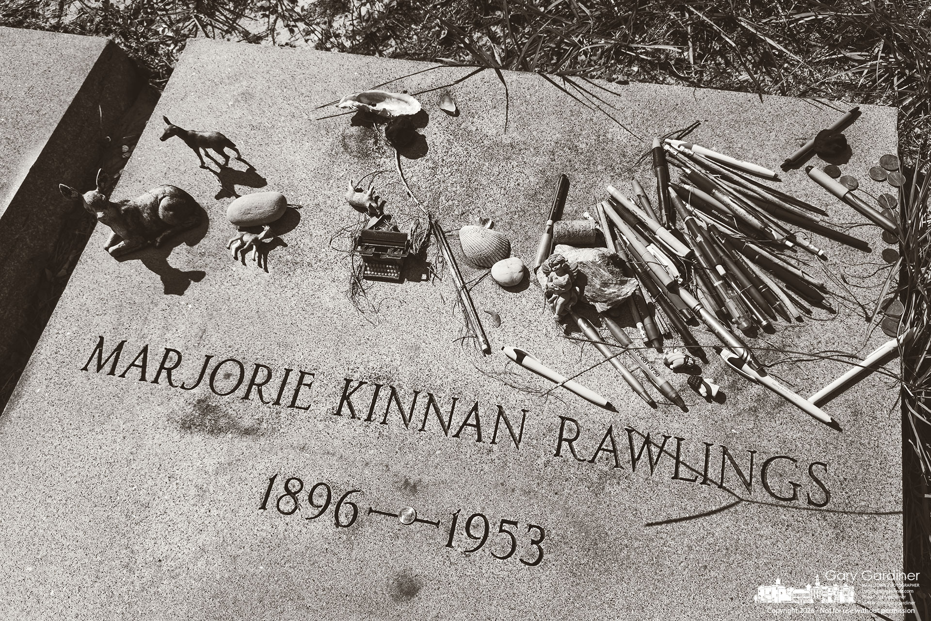 A collection of ephemera, pens, and pencils sits on the gravestone for Marjorie Kinnan Rawlings, several miles from her Cross Creek home. (My Final Photo for October 20, 2026. Photo by Gary Gardiner)