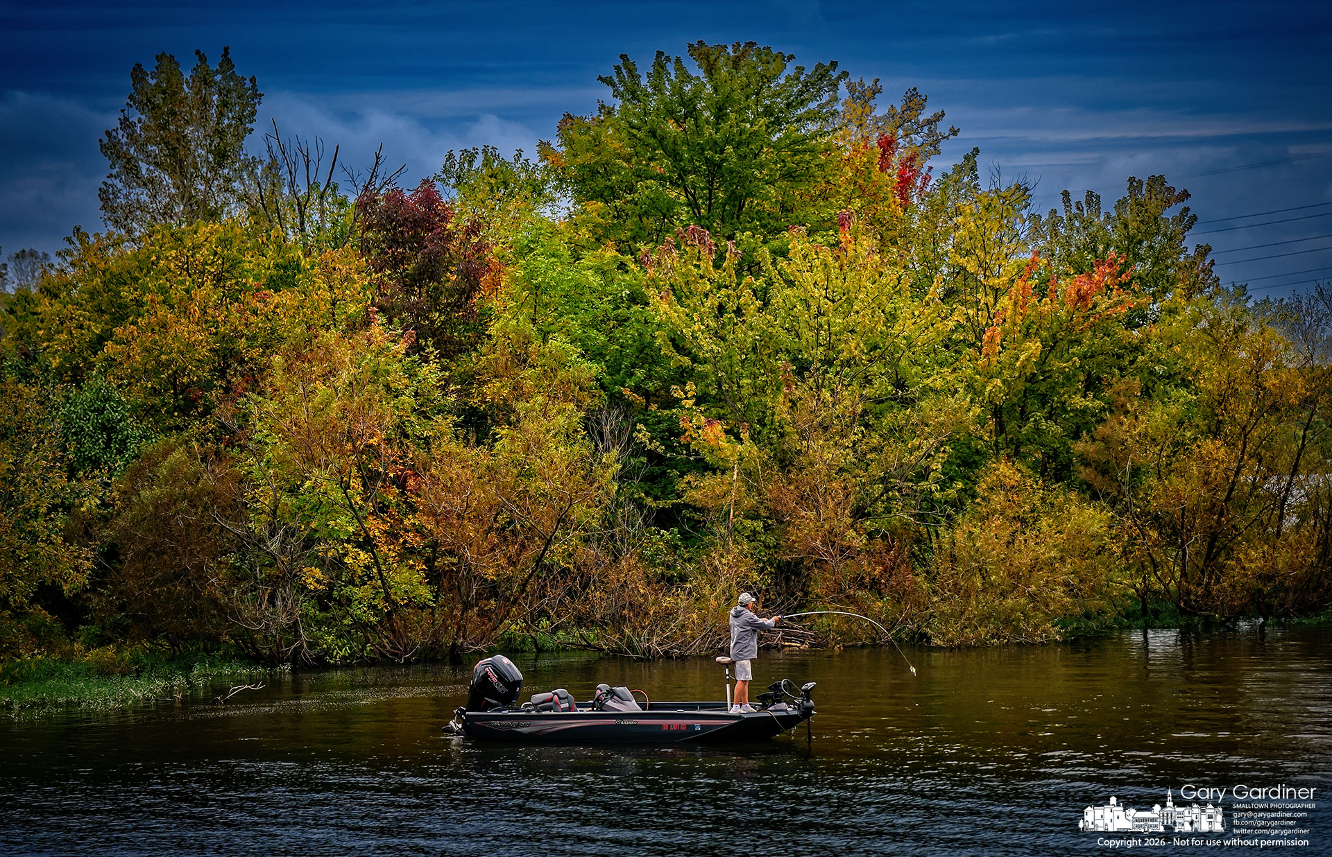 An angler steers his boat along the Hoover Reservoir shoreline, where the trees and brush have begun to turn fall colors. (My Final Photo for October 2, 2026. Photo by Gary Gardiner)
