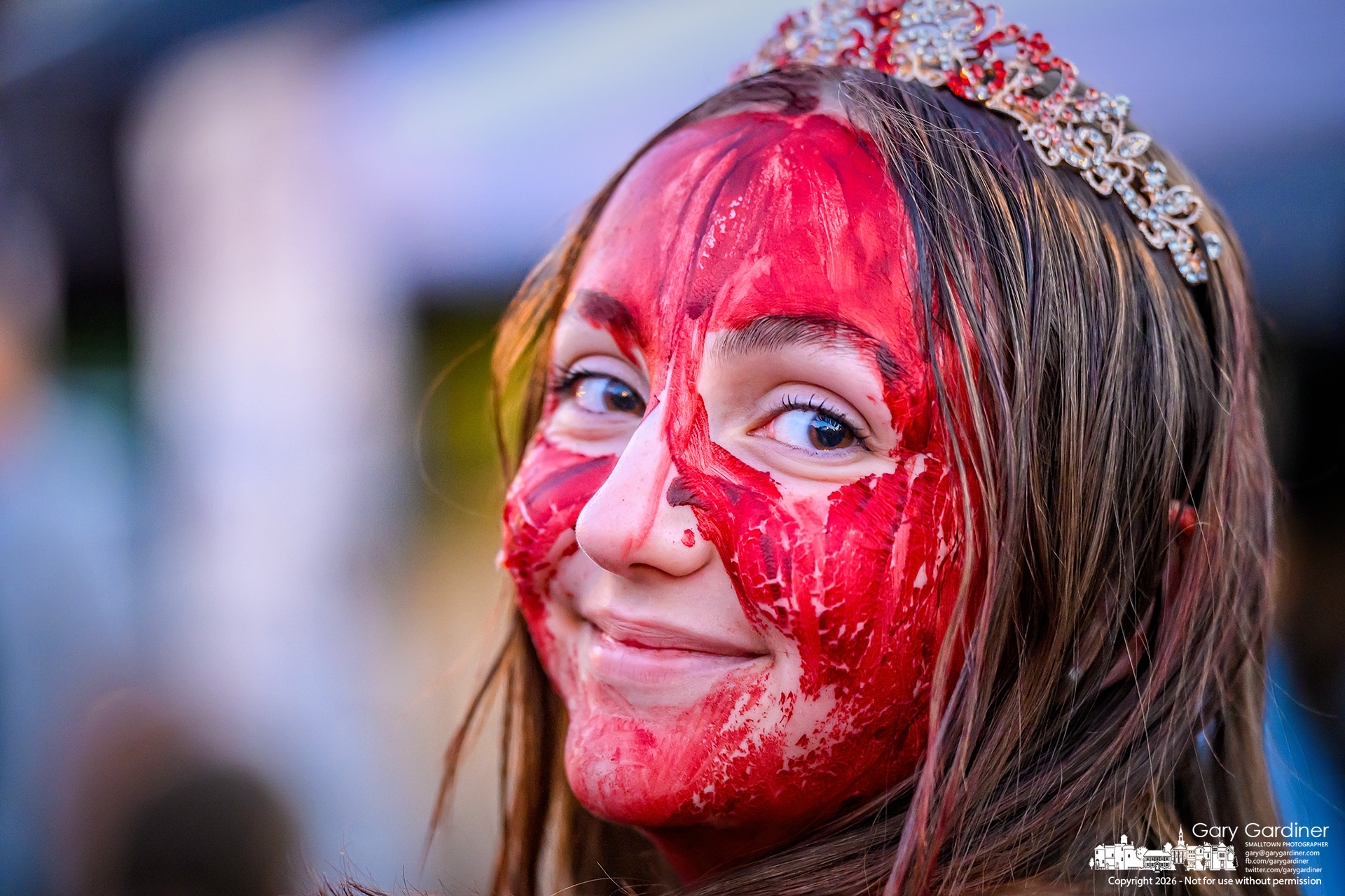 A young girl dressed as another generation of Carrie wears an innocent grin as she walks through Midnight Madness in Uptown. (My Final Photo for October 23, 2026. Photo by Gary Gardiner)